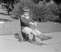 A young child playing outside on a small wooden scooter ca.  between 1918 and 1920
