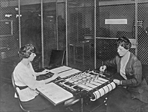 Two women using check signing machine which signs checks issued by the War Risk Bureau, Washington, D.C. ca. between 1909 and 1932