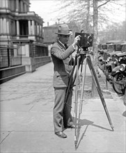 Man using a motion picture camera on a tripod, possibly a Debrie or Parvo L camera ca. between 1909 and 1923