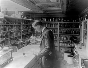Pharmacist at People's Drug Store, No. 5, 8th and H Streets, N.E., Washington, D.C., looking at prescriptions on the counter ca. between 1909 and 1932