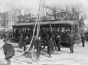 Firemen with hoses stretched over a streetcar ca. 1909