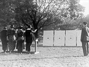 Four policewomen shooting at targets, as a policeman watches ca. 1909