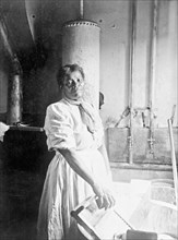 African American woman, three-quarter length portrait, standing, facing front, doing laundry ca. 1909