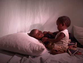 Children in Africa are protected from malaria when they sleep under a bed net; two children playing in a bed under a net; ca. 24 February 2005