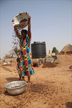 A Ghanian woman in a colorful dress pouring what looks to be nuts into a bowl in a small village in Northern Ghana ca. 20 February 2018