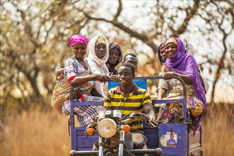 A man driving a motorcycle cart ferries West Africa village women ca. 21 February 2018