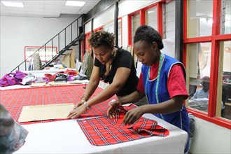 Woman working on Masai fabrics which are hand cut in preparation for custom made Doreen Mashika handbags. Each of these products are designed, manufactured, and produced by Africans, possibly in Kenya...