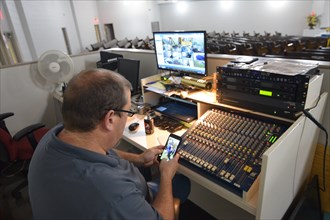 During the Covid-19 pandemic, some churches chose to record sermons to play on their websites and through streaming services to replace in person worship. Here, a deacon in the sound booth looks at hi...