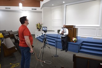 During the Covid-19 pandemic, some churches chose to record sermons to play on their websites and through streaming services to replace in person worship. Here, a technician records a minister as he p...