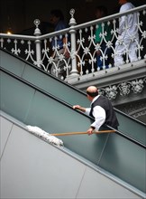 Worker at the Crescent Court Hotel in Dallas, TX; man cleaning with dust mop, riding an escalator