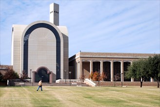 Student walking across a grass field in front of the Bible building at Abilene Christian University