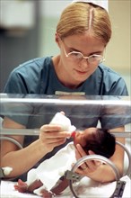 A nurse feeds an infant in an incubator.