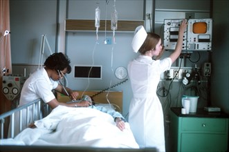 A nurse examines a patient while another nurse adjusts a monitor.
