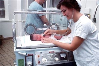 A nurse examines an infant in an incubator.