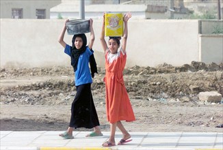 Two young Iraqi girls carry buckets full of water