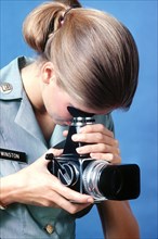 A female U.S. Army photographer demonstrates the use of a 70mm camera.
