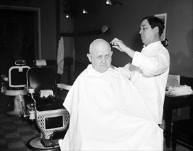 An almost bald man receiving a hair cut in a barber shop