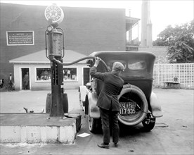 Man pumping gas into his automobile in early 1900s