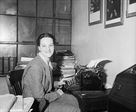 Woman in office sitting at a typewriter looking at camera smiling
