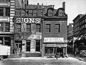 1930s New York City - Sign company with decorative ironwork along roof, auto radiator shop, in three-story buildings, the elevated railroad just visible at right. Broome Street, Nos. 504-506, Manhatta...