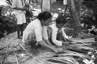 Street scenes. Woman and boy busy braiding a screen of atap leaves; Date 24 August 1948 Location Indonesia, Dutch East Indies