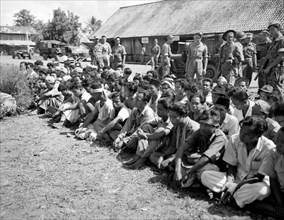 Indonesia History - Indonesian prisoners of war or detainees sit in lotus seat on the ground guarded by Dutch soldiers