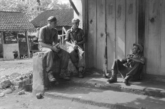 Operation Schoonschip. Three soldiers are resting in front of a building in a kampong; Date March 29, 1949; Location Indonesia, Dutch East Indies