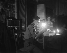 A soldier opens a package by candlelight and light from an oil lamp; Date 1947; Location Indonesia, Dutch East Indies
