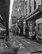 1937 New York City street scene - Allen Street, no. 55-57, Manhattan. Under the shadow of the elevated railroad visible at the left are dress, underwear, drapery and bedding manufacturers and stores.