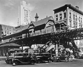 Elevated railroad station in Hanover Square in Lower Manhattan, cars below, buildings of various eras beyond ca. 1936