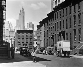 1930s New York City - Laundry wagon, cars, along sloping street lined with rowhouses, skyline of Manhattan visible above buildings at end of the street ca. 1936