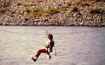 Ca. 1975 - Man using zipline to cross Resurrection River, Alaska
