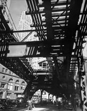 View of the elevated railroad station in Hanover square from below the tracks, skyscrapers visible between the tracks ca. 1936
