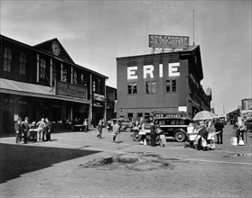 Traffic and vendors in front of Erie Railroad ferry, terminal at left, other building center ca. 1938