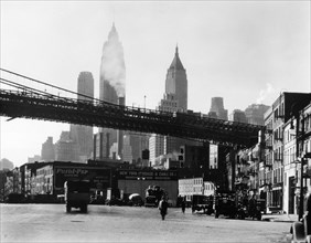 Brooklyn Bridge span as it reaches land above South Street near James, tall buildings rise beyond ca. 1935