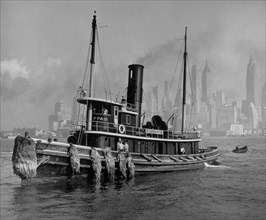 Looking broadside at the tugboat Watuppa, with the lower Manhattan (from the Municipal Bldg. south) skyline in the background ca. 1936