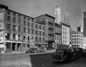 Dey Street between West and Washington Streets, Manhattan. Express companies, ships' outfitters and a contractor fill 4 and 5 story buildings along Dey St., tall towers beyond in upper right. ca. 1936