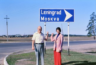 Tourists in Russia during the late 1970s pointing at a road sign for Moscow and Leningrad ca. 1978