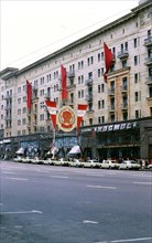 Large hammer and sickle banner outside a building in the Soviet Union in the late 1970s (1978), rows of similar white Russian cars parked in front