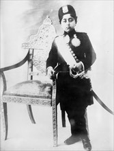 Shah of Persia, in uniform, standing by chair