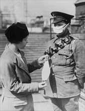 British soldier wearing a face mask to protect against poison gas, standing with a woman holding another face mask, during World War I ca. 1914-1915