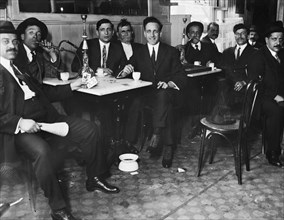 Men sitting inside a Syrian restaurant, man on the right smoking on a hookah pipe ca. 1910-1915