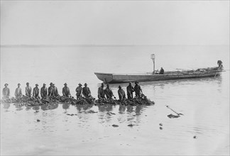 African American fishermen standing in water near a boat ca. 1910-1915