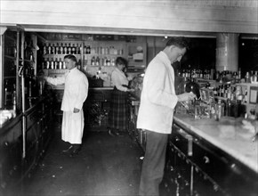 Pharmacists at People's Drug Store, 7th and E Streets, N.E., Washington, D.C., at counter preparing medications ca. 1909-1932