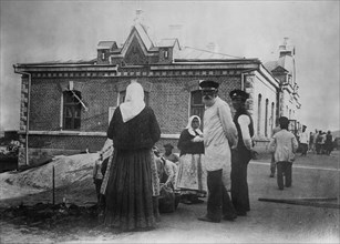 Russian peasant women and men standing outside a brick building, probably during World War I ca. 1914
