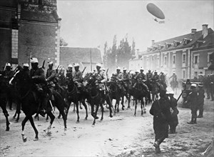 French soldiers on horseback in street, with airship Dupuy de Lome flying in air behind them during World War I ca. 1914-1915