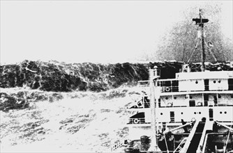 Merchant ship laboring in heavy seas as huge wave looms astern.Huge waves are common near the 100-fathom curve on the Bay of Biscay - Atlantic Ocean, Bay of Biscay ca. 1940