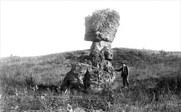 August 28th, 1901 photo of a gentleman with his hand on a leaning tower of St. Peter Sandstone as a result of post-glacial weathering near Footville, Wisconsin. (Leaning tower of rock).