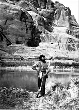 John F. Steward, a member of the Powell Survey, in Glen Canyon, Colorado River. He is shown with the typical field equipment of those early Surveys: gun, pick, map case, and a canteen. This photo was ...