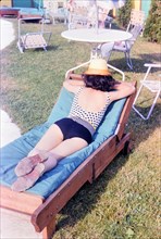 Woman sunbathing outdoors, lying on her stomach, wearing a hat 1966